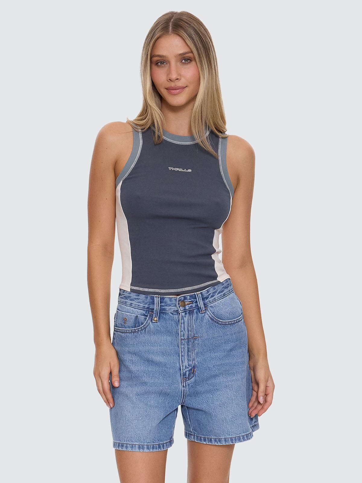 Woman wearing a sleeveless gray top with a logo and denim shorts on a light gray background